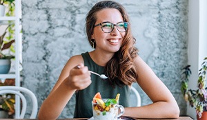 Woman with glasses smiling and enjoying yogurt with fruit