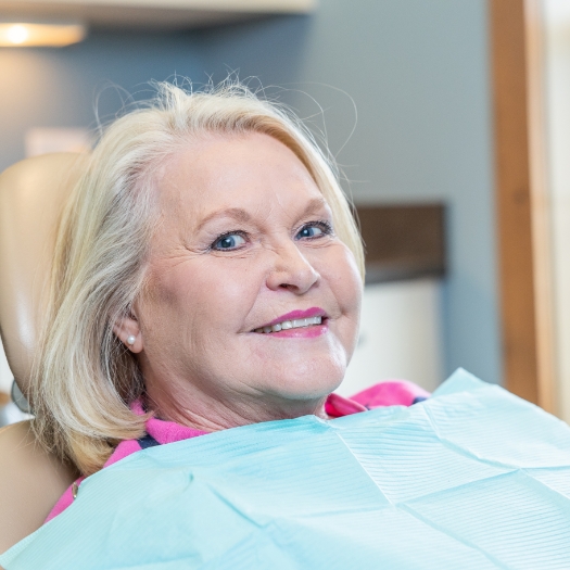 Woman pointing to smile after metal free dental restoration treatment