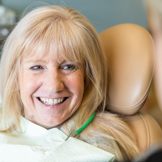 young woman admiring results of her dental treatment in hand mirror 