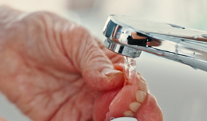 Hand holding a denture under running water in a sink