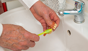 Person cleaning their denture with a toothbrush