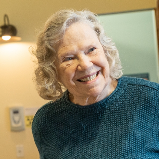 A middle-aged woman seated on an outdoor bench and smiling because of her new denture