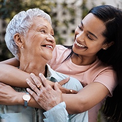 A smiling mother and daughter hugging outdoors