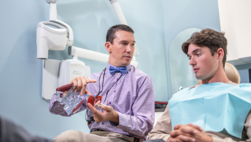 Doctor Parry holding a model of the mouth while talking to a patient