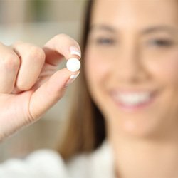 A woman holding a round pill between her fingers