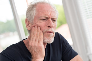 Older man rubbing jaw due to TMJ pain